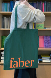 Mid-length photo of person holding Faber tote bag with bookcase behind